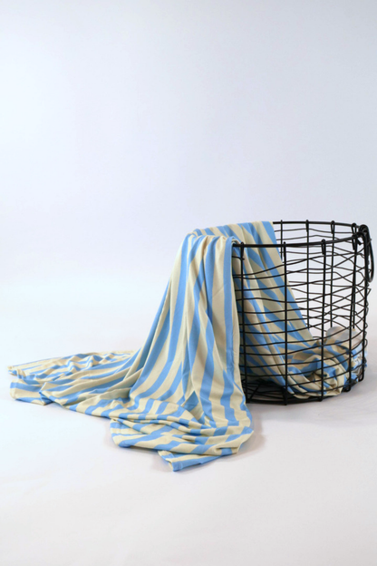 Our Coastal Stripes swaddle features soft blue and cream vertical stripes. It is shown featured over a black wire basket.