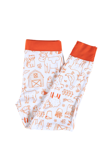 Our two-piece Barnyard Buddies jammies are a charming farm-inspired design featuring a variety of animals including cows, chickens, horses, dogs, cats and more across a white background with matching orange cuffs and trim.